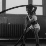 Woman in a gym engaging in vigorous battle rope workout for fitness.