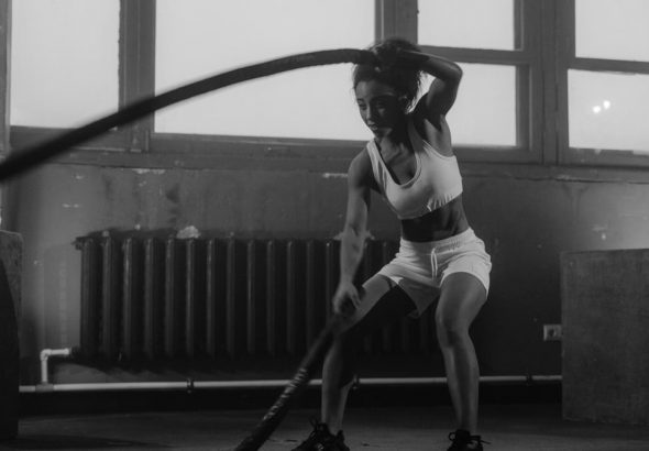 Woman in a gym engaging in vigorous battle rope workout for fitness.